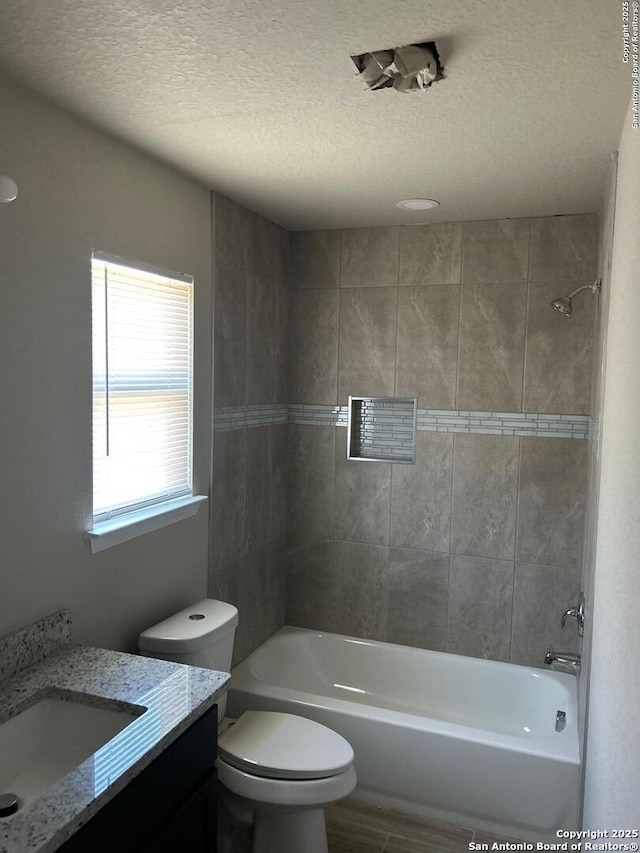 full bathroom featuring a textured ceiling, vanity, toilet, and tiled shower / bath combo