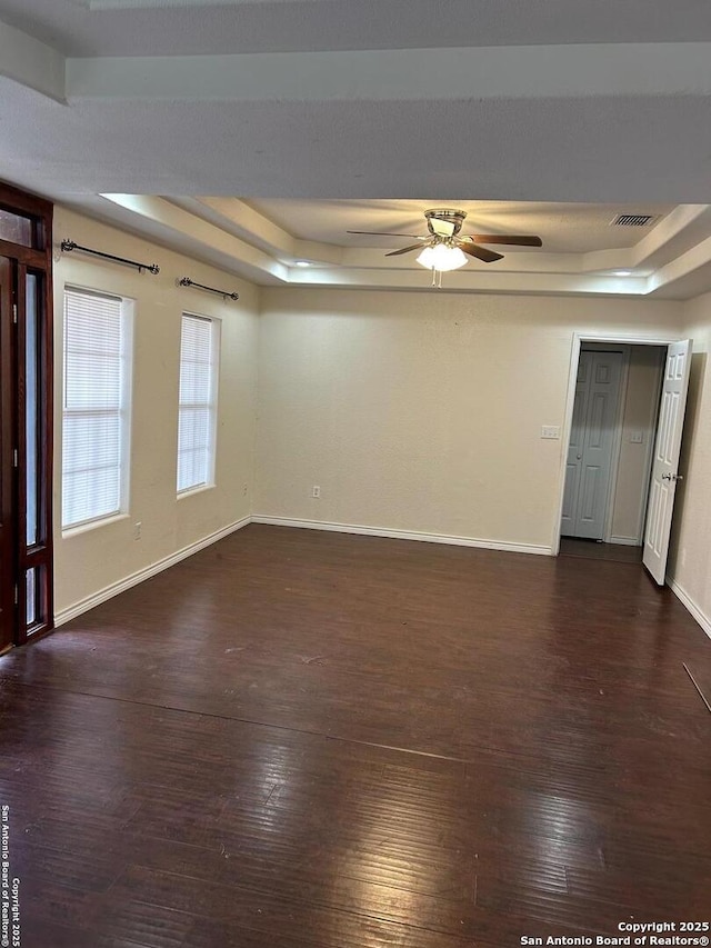 empty room with dark hardwood / wood-style floors, a raised ceiling, and ceiling fan