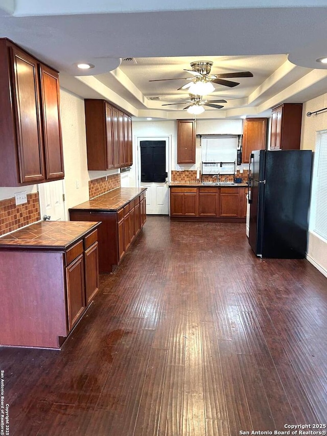 kitchen with a raised ceiling, black fridge, tasteful backsplash, and sink