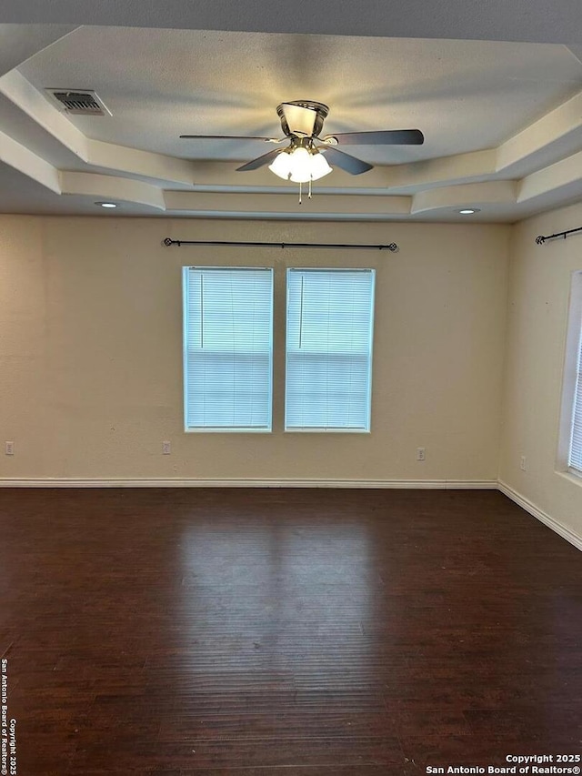 unfurnished room with a textured ceiling, dark hardwood / wood-style flooring, a tray ceiling, and ceiling fan