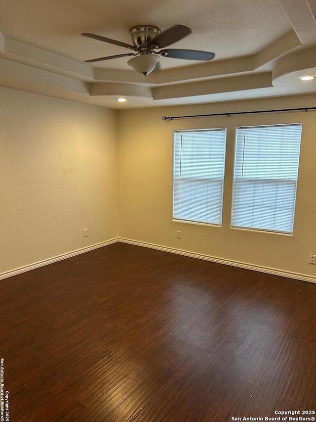 spare room featuring a raised ceiling, ceiling fan, and dark hardwood / wood-style floors