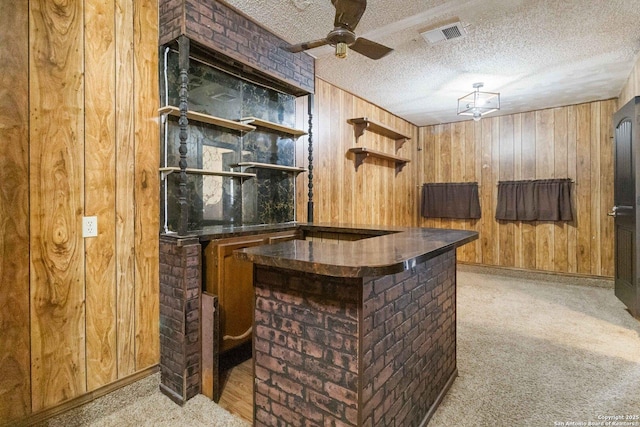 bar with light carpet, ceiling fan, wooden walls, and a textured ceiling