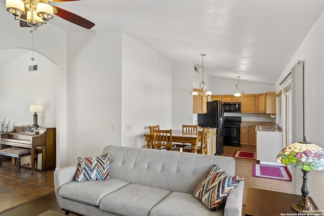 living room with ceiling fan with notable chandelier, vaulted ceiling, and dark tile patterned floors