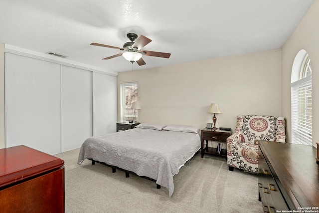 bedroom with ceiling fan, light carpet, and a closet