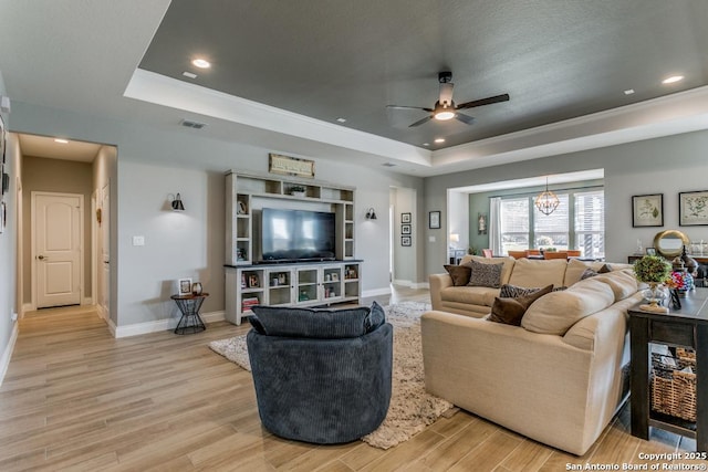 living room featuring ceiling fan with notable chandelier, light hardwood / wood-style floors, and a tray ceiling