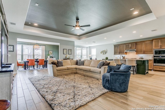 living room with a raised ceiling, a textured ceiling, and ceiling fan with notable chandelier