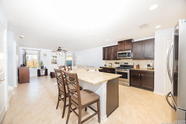 kitchen featuring appliances with stainless steel finishes, ceiling fan, a kitchen island with sink, sink, and a breakfast bar area