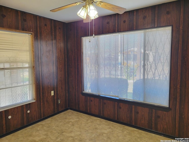 unfurnished room with a healthy amount of sunlight, ceiling fan, and wooden walls