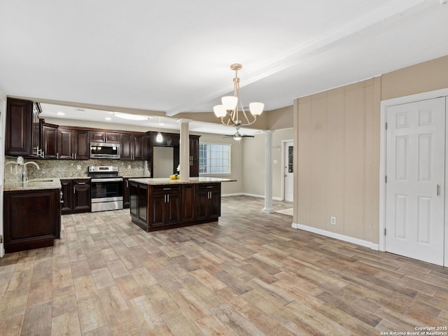 kitchen with hanging light fixtures, ornate columns, appliances with stainless steel finishes, a kitchen island, and dark brown cabinetry