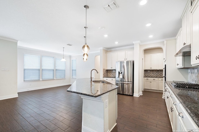 kitchen featuring a kitchen island with sink, dark stone counters, sink, decorative light fixtures, and stainless steel appliances