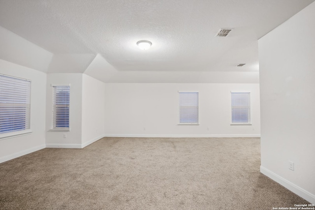 unfurnished room with a textured ceiling, carpet floors, and lofted ceiling