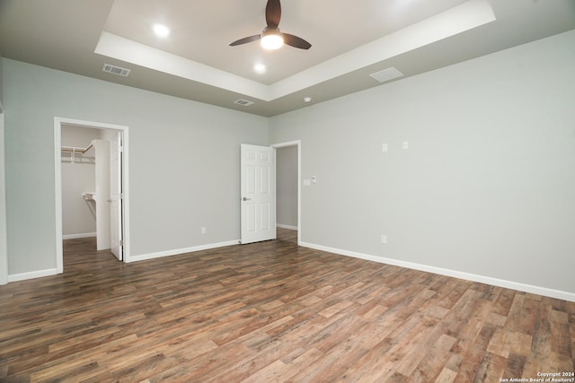 unfurnished bedroom with a tray ceiling, ceiling fan, a spacious closet, dark hardwood / wood-style floors, and a closet