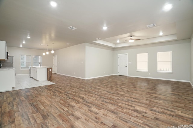 unfurnished living room featuring ceiling fan, light hardwood / wood-style floors, a raised ceiling, and sink