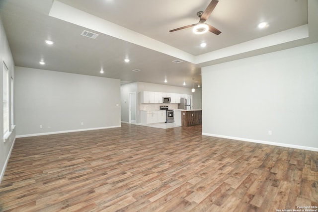 unfurnished living room featuring ceiling fan, light hardwood / wood-style floors, and a raised ceiling