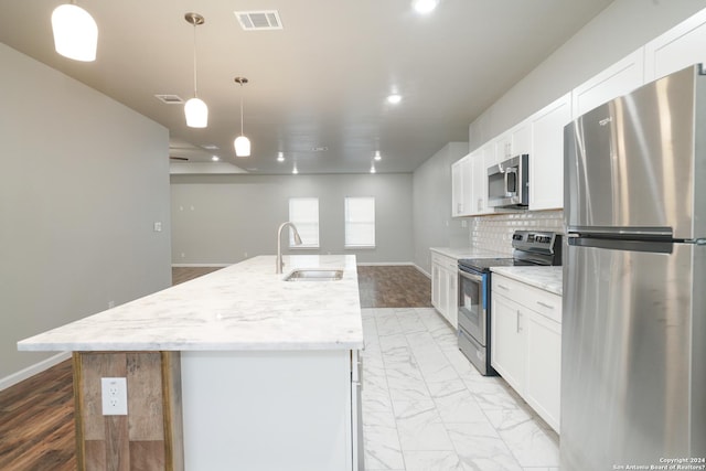 kitchen featuring stainless steel appliances, sink, decorative light fixtures, white cabinetry, and an island with sink