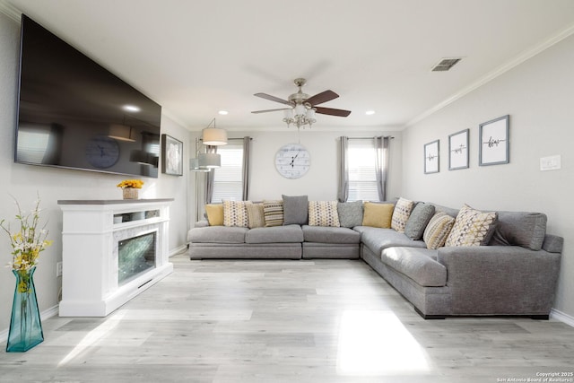 living room with a fireplace, light hardwood / wood-style flooring, ceiling fan, and ornamental molding