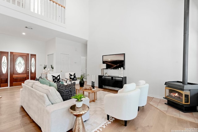 living room featuring light wood-type flooring, a towering ceiling, and a wood stove