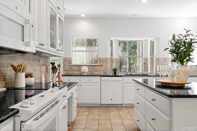 kitchen featuring white appliances, dark stone counters, sink, light tile patterned floors, and white cabinetry