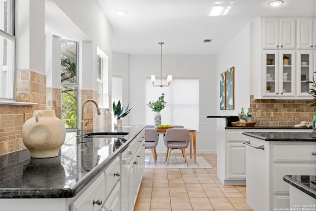 kitchen featuring a center island, sink, dark stone countertops, pendant lighting, and white cabinets