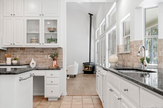 kitchen with white cabinets, a wood stove, sink, and light tile patterned floors