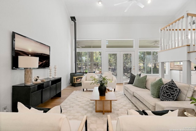 living room with a wood stove, french doors, ceiling fan, ornamental molding, and wood-type flooring