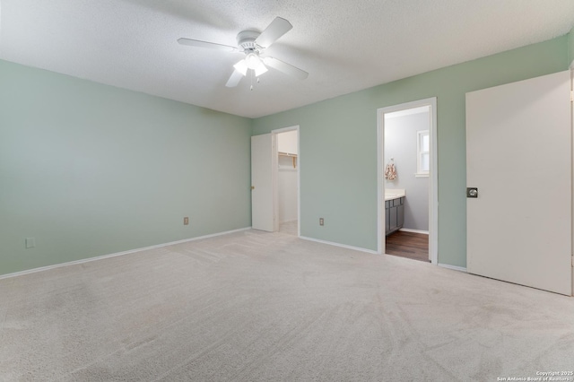 unfurnished bedroom featuring light carpet, a walk in closet, ensuite bath, a textured ceiling, and ceiling fan