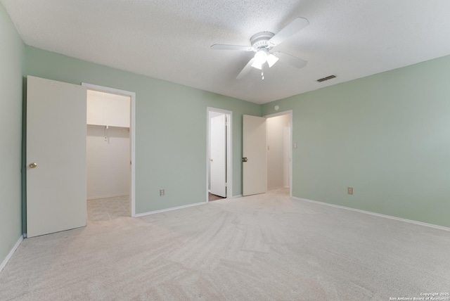 unfurnished bedroom with ceiling fan, a spacious closet, a textured ceiling, light colored carpet, and a closet