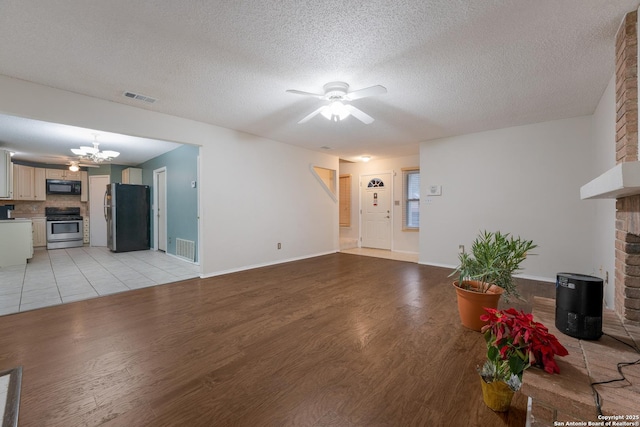 unfurnished living room with ceiling fan with notable chandelier, light hardwood / wood-style floors, a textured ceiling, and a brick fireplace