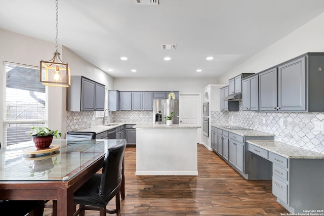 kitchen with stainless steel appliances, dark wood-type flooring, pendant lighting, gray cabinets, and a kitchen island