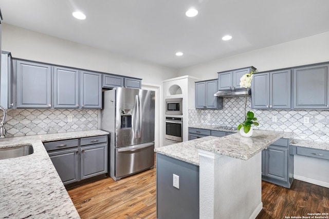 kitchen featuring sink, a center island, dark wood-type flooring, light stone counters, and appliances with stainless steel finishes