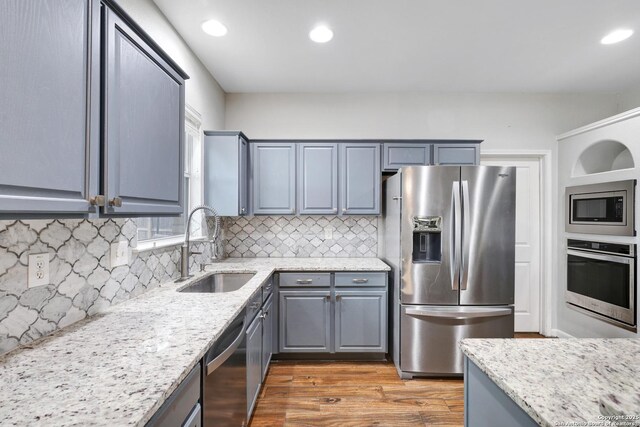 kitchen with appliances with stainless steel finishes, tasteful backsplash, light stone counters, and sink