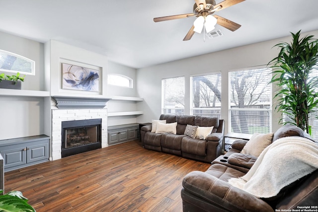 living room with a fireplace, ceiling fan, and dark wood-type flooring