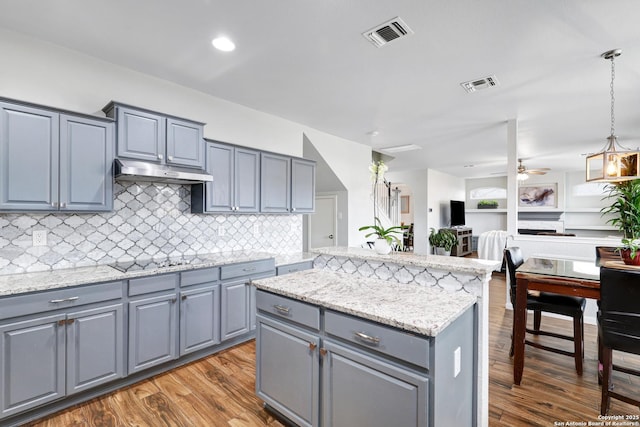 kitchen featuring black electric stovetop, ceiling fan, hardwood / wood-style floors, a kitchen island, and hanging light fixtures