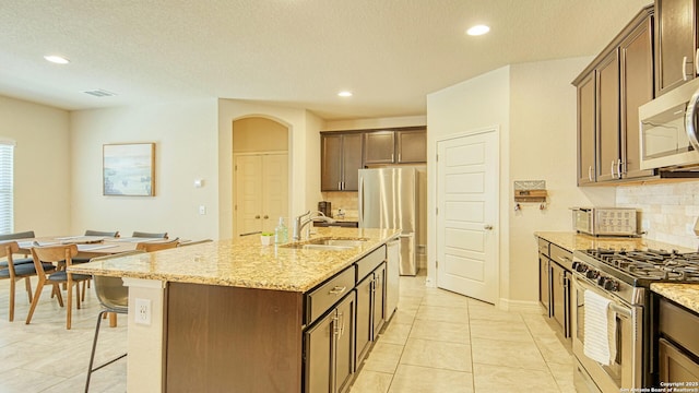 kitchen with sink, light stone counters, an island with sink, light tile patterned floors, and appliances with stainless steel finishes