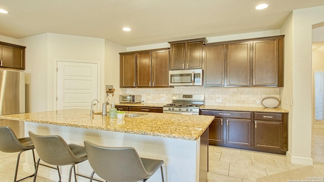 kitchen featuring sink, tasteful backsplash, a center island with sink, light tile patterned floors, and appliances with stainless steel finishes