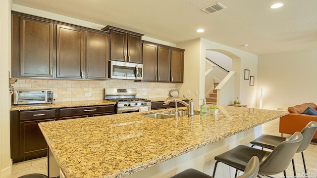 kitchen featuring appliances with stainless steel finishes, backsplash, a kitchen breakfast bar, a kitchen island with sink, and sink