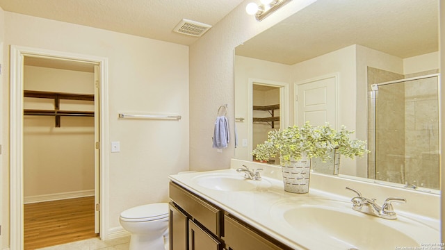 bathroom featuring tile patterned flooring, a textured ceiling, toilet, a shower with door, and vanity