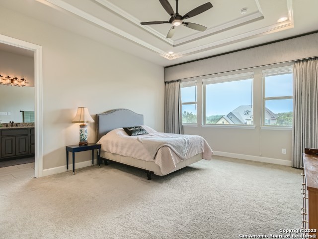 bedroom with ceiling fan, sink, a raised ceiling, ensuite bathroom, and light carpet