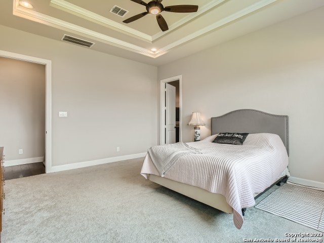 carpeted bedroom featuring a tray ceiling, ceiling fan, and ornamental molding