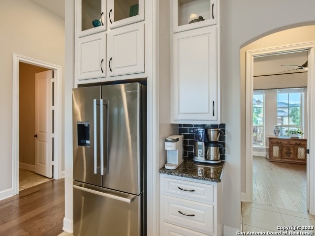 kitchen featuring backsplash, light wood-type flooring, dark stone counters, white cabinets, and stainless steel fridge with ice dispenser