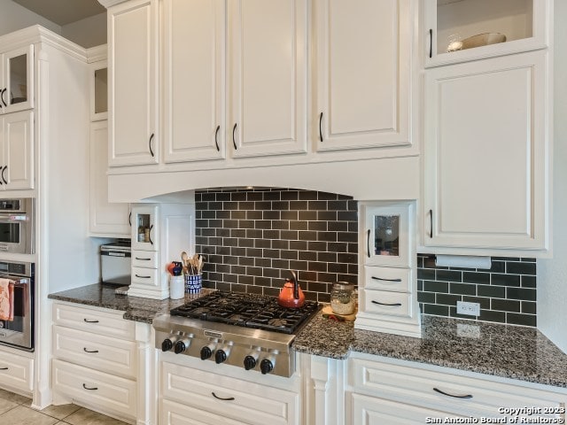 kitchen with decorative backsplash, appliances with stainless steel finishes, white cabinetry, and dark stone counters