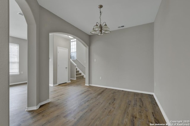 empty room with a wealth of natural light, hardwood / wood-style floors, and a notable chandelier