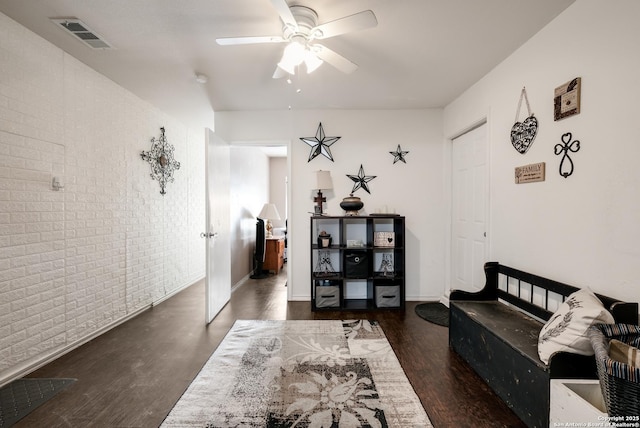 living room with dark hardwood / wood-style floors, ceiling fan, and brick wall