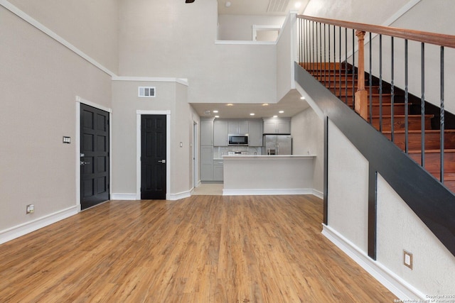 unfurnished living room featuring a towering ceiling and light hardwood / wood-style floors