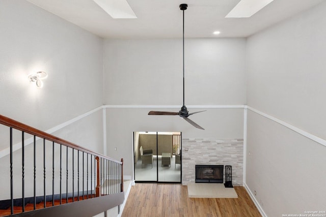 unfurnished living room with ceiling fan, a skylight, a fireplace, and wood-type flooring