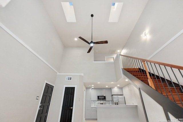 unfurnished living room featuring ceiling fan, a skylight, and a high ceiling