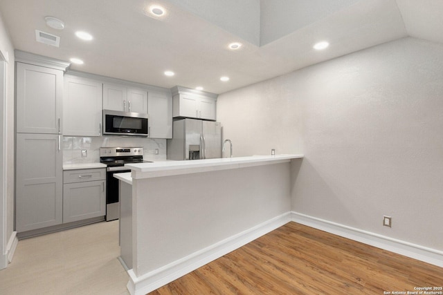 kitchen with stainless steel appliances, vaulted ceiling, light hardwood / wood-style floors, backsplash, and gray cabinetry