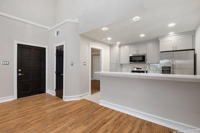 kitchen with kitchen peninsula, stainless steel appliances, light hardwood / wood-style floors, and white cabinetry