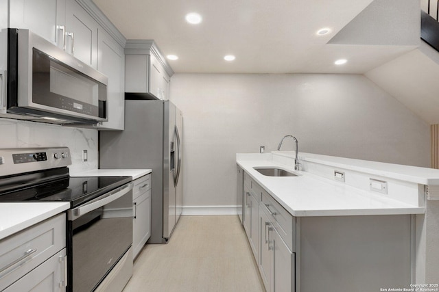 kitchen featuring kitchen peninsula, decorative backsplash, gray cabinets, appliances with stainless steel finishes, and sink