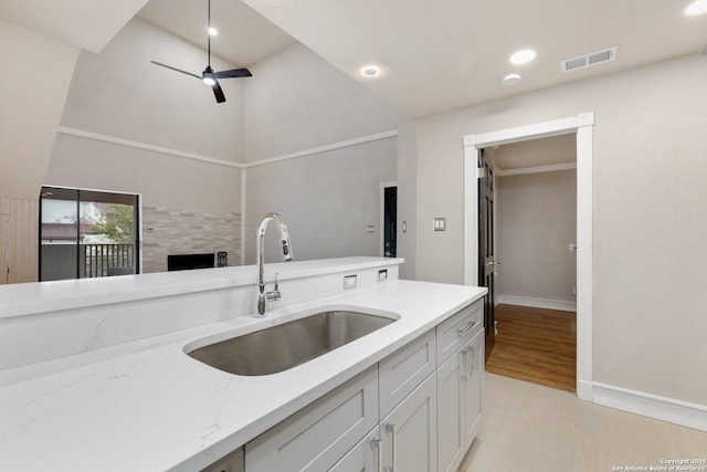 kitchen featuring light stone countertops, white cabinetry, a fireplace, ceiling fan, and sink